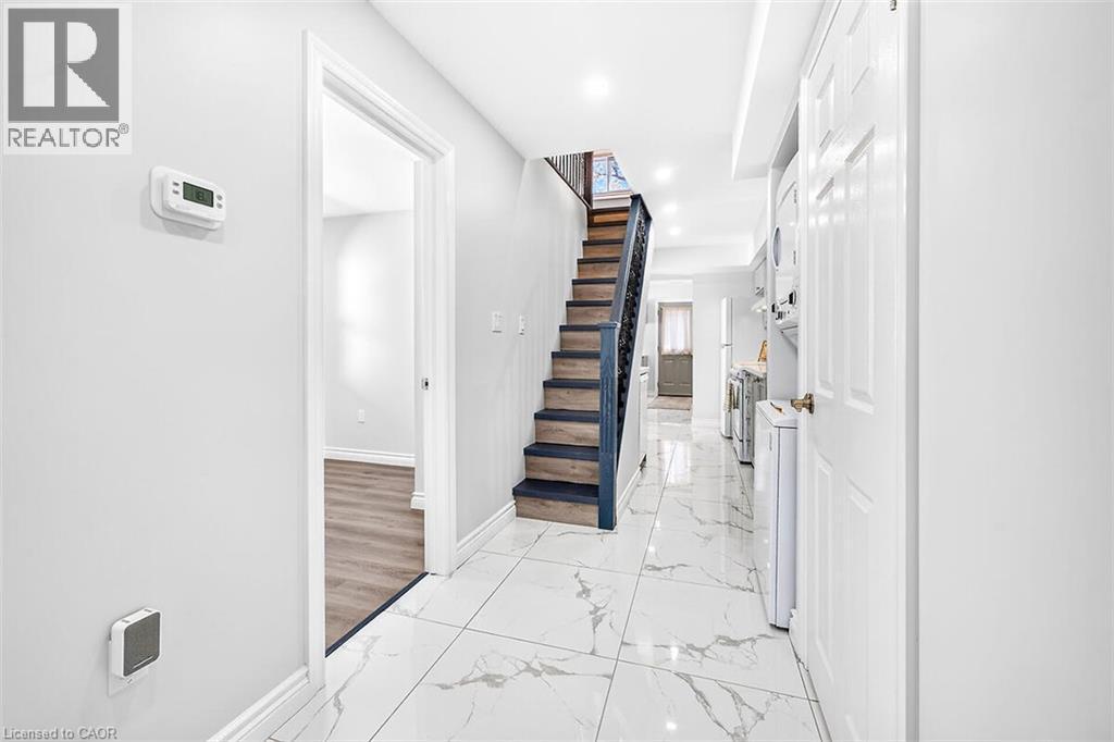 White tile flooring, wood-finish stairs with dark railing, white walls, and a visible doorway - 4 Albemarle Street, Hamilton, ON