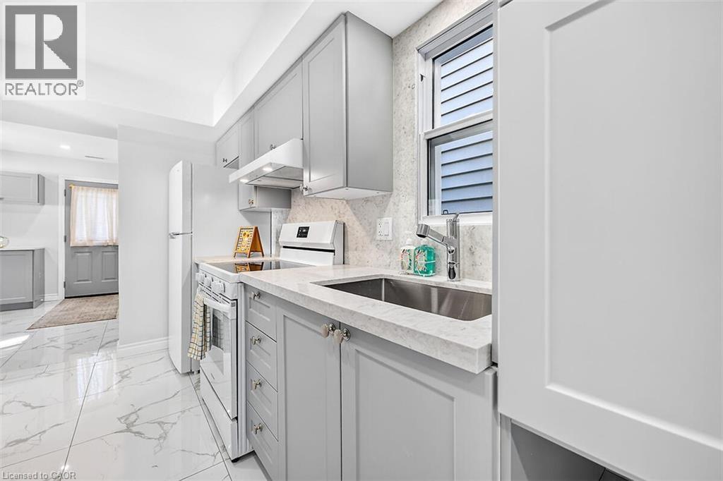 Light gray cabinetry with brushed nickel hardware, white stone countertops, stainless steel undermount sink, white tile flooring with gray veining, and white appliances - 4 Albemarle Street, Hamilton, ON