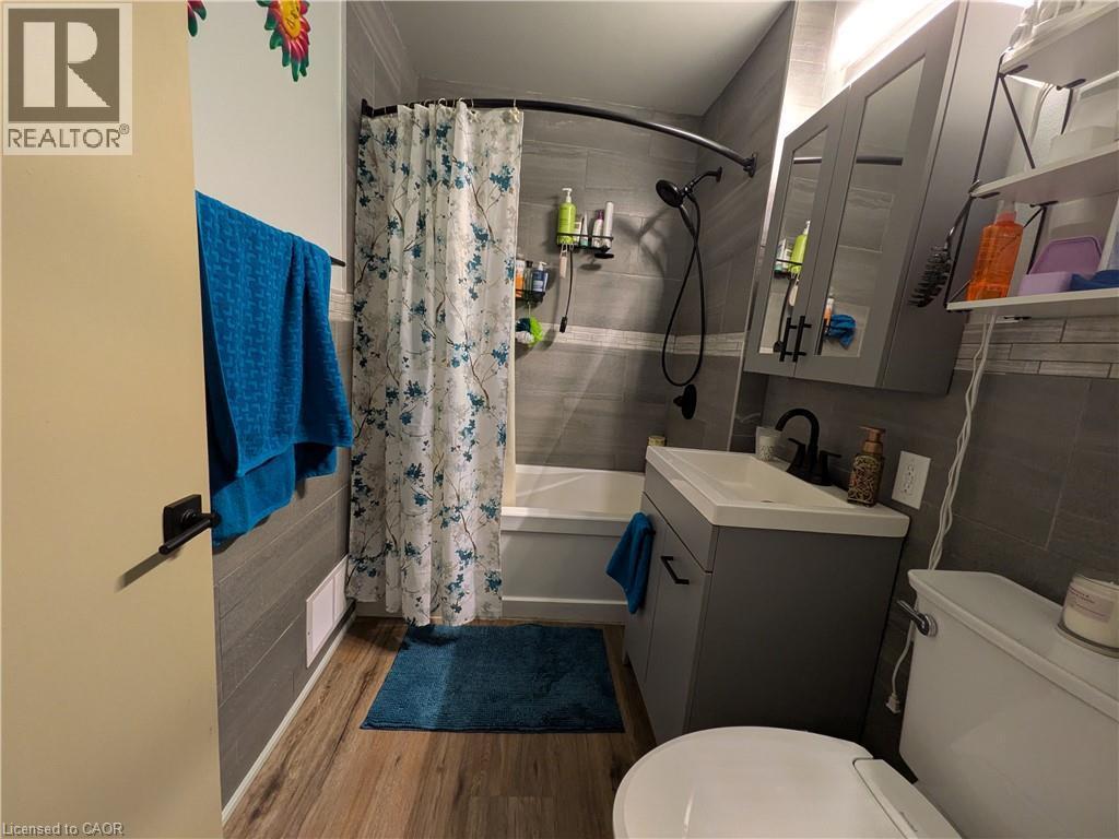 Wood-finish flooring with a white bathtub and tiled shower surround - 487 Scholfield Avenue N, Welland, ON
