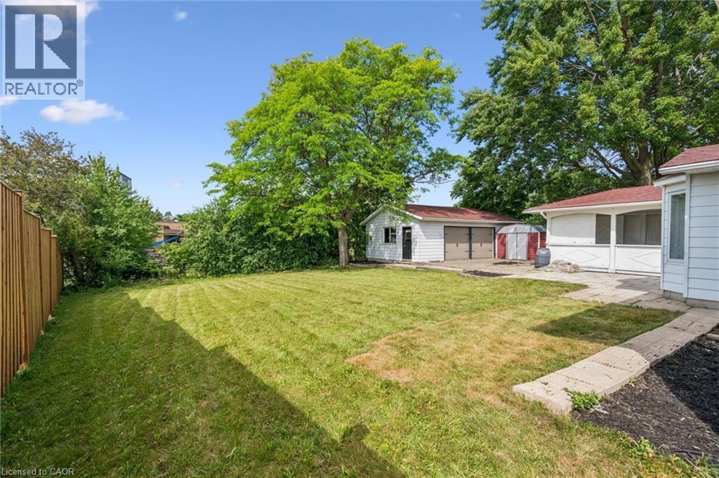 Expansive backyard featuring a large grass area, mature trees, a detached two-car garage with red roofing, a single-car garage, and a concrete patio - 299 Dale Crescent, Waterloo, ON