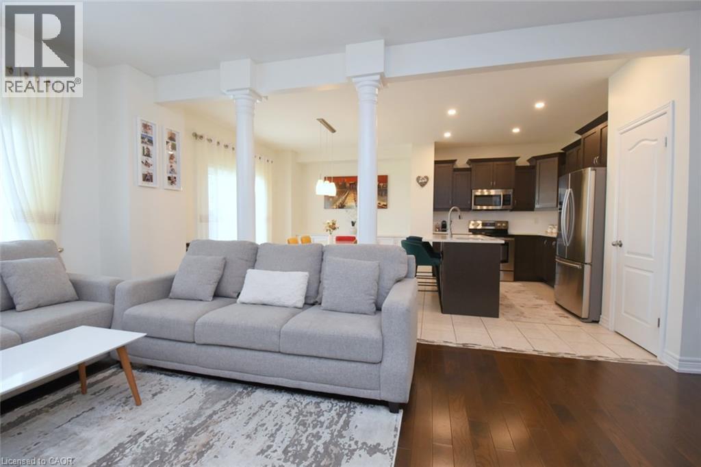 Open-concept living space featuring wood-finish flooring, recessed lighting, white walls, and a kitchen with dark cabinetry and stainless steel appliances - 25 Guest Street, Hamilton, ON