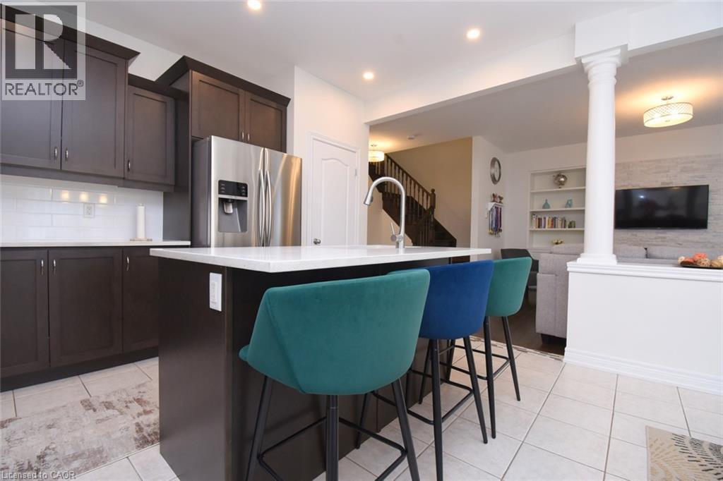 Kitchen featuring dark wood-finish cabinetry, a white countertop island with an integrated sink, stainless steel refrigerator, and tiled flooring - 25 Guest Street, Hamilton, ON