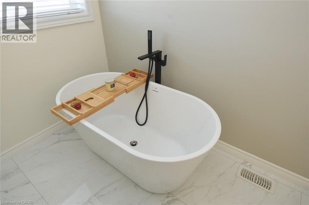 Freestanding soaking tub with a matte black floor-mounted faucet and handheld shower sprayer - 25 Guest Street, Hamilton, ON