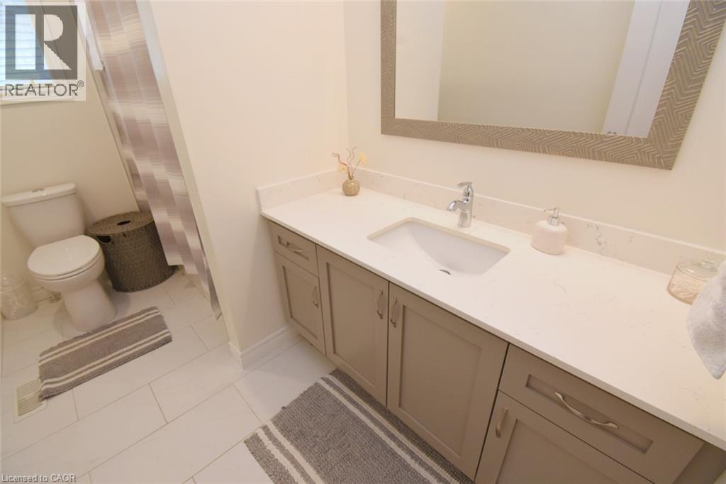 Single vanity with a light countertop, integrated sink, chrome faucet, and cabinet storage - 25 Guest Street, Hamilton, ON