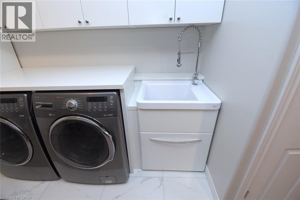 White upper cabinetry, white countertops, built-in utility sink with a flexible chrome faucet, and white floor tiling - 25 Guest Street, Hamilton, ON