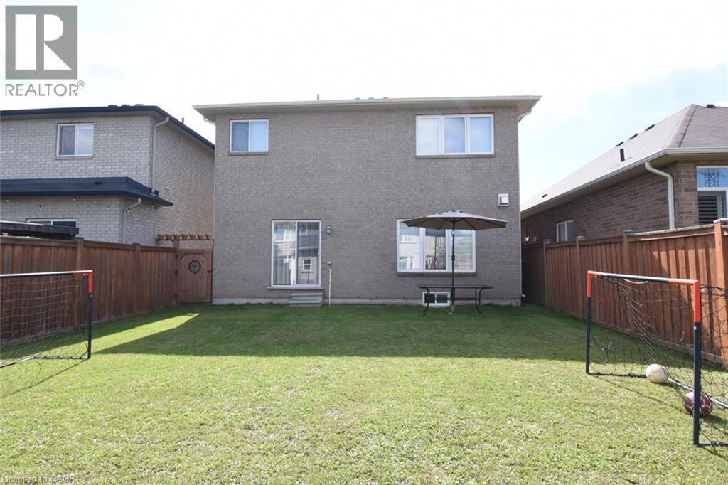 Expansive rear yard featuring a grass lawn, wood fencing, and a rear door with an exterior light fixture - 25 Guest Street, Hamilton, ON