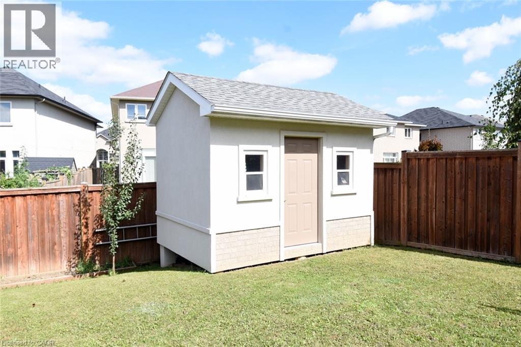 Detached storage shed with dual windows and a paneled door, set within a fenced yard featuring wood privacy fencing and a manicured lawn - 25 Guest Street, Hamilton, ON