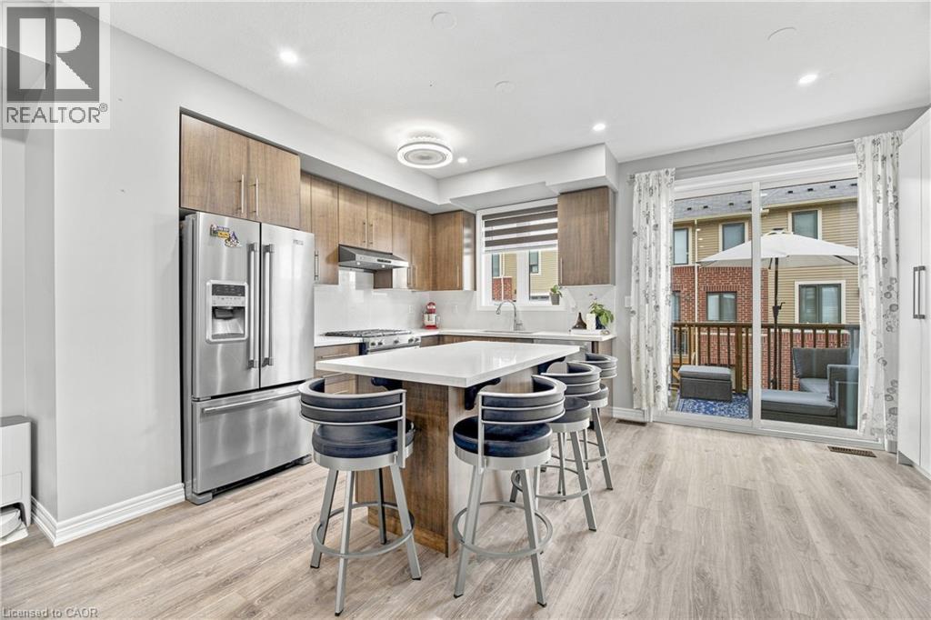 Modern kitchen featuring wood-finish cabinetry, stainless steel appliances, a white countertop island, and wood-finish flooring - 1890 Rymal Road E Unit# 144, Hamilton, ON