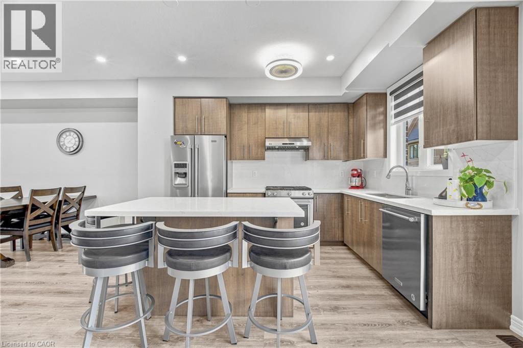 Contemporary kitchen featuring wood-finish cabinetry, stainless steel appliances, a white tile backsplash, a center island with seating, and wood-finish flooring - 1890 Rymal Road E Unit# 144, Hamilton, ON