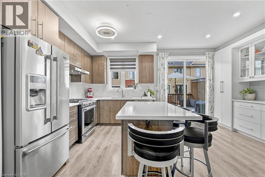 Contemporary kitchen featuring wood-finish cabinetry, stainless steel appliances, a white island countertop, and light wood-look flooring - 1890 Rymal Road E Unit# 144, Hamilton, ON