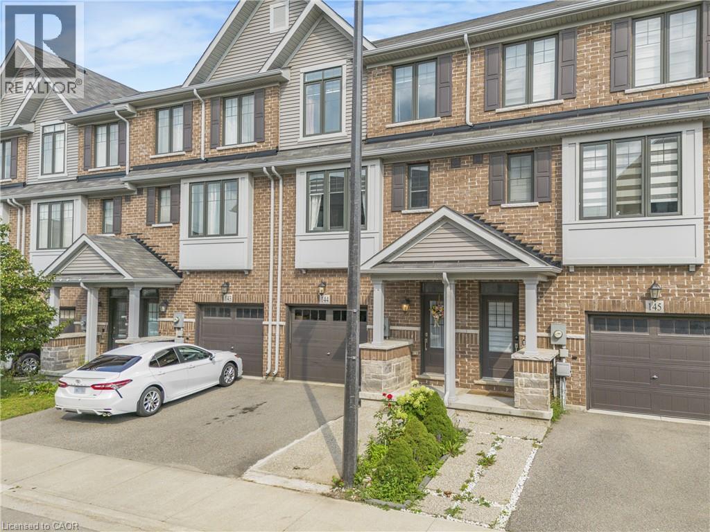 Brick exterior with gabled roofline, multiple windows with dark shutters, covered entry, and attached garage - 1890 Rymal Road E Unit# 144, Hamilton, ON