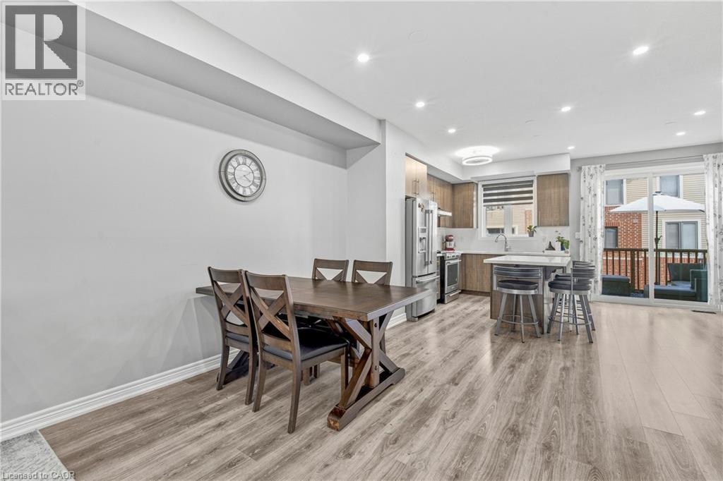 Open-concept living area with wood-finish flooring, recessed lighting, and a modern kitchen featuring stainless steel appliances, a center island with seating, and wood-finish cabinetry - 1890 Rymal Road E Unit# 144, Hamilton, ON
