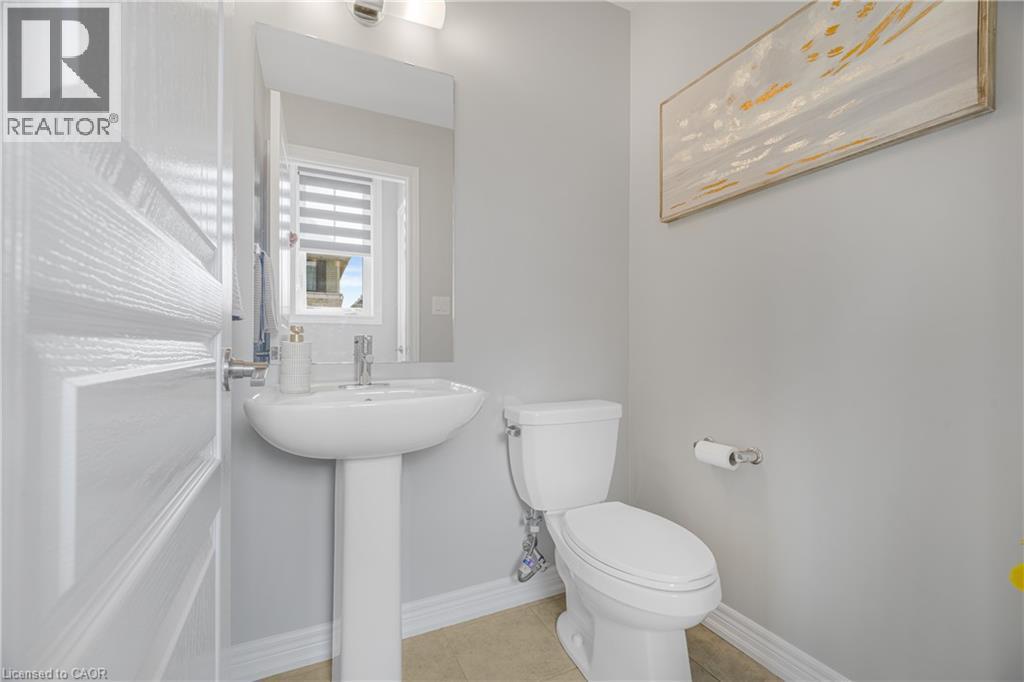 Pedestal sink with chrome faucet, wall-mounted mirror, overhead vanity lighting, and a window with blinds - 1890 Rymal Road E Unit# 144, Hamilton, ON