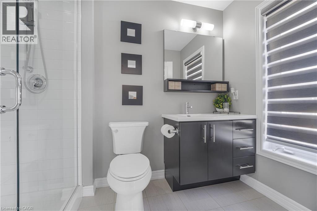 Modern bathroom featuring a glass-enclosed shower, dark wood-finish vanity with chrome pulls, integrated sink, and large wall-mounted mirror - 1890 Rymal Road E Unit# 144, Hamilton, ON