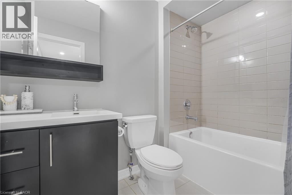 White undermount sink with a chrome faucet, dark wood-finish vanity with chrome hardware, rectangular mirror, and a white bathtub with horizontal tile surround - 1890 Rymal Road E Unit# 144, Hamilton, ON