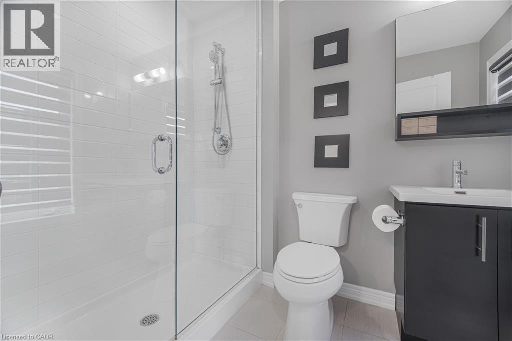 Glass-enclosed shower with white subway tile, chrome shower fixture, single vanity with dark cabinetry, integrated sink, and wall-mounted mirror - 1890 Rymal Road E Unit# 144, Hamilton, ON
