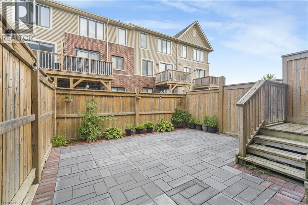 Private patio featuring paver stones with brick-finish border, wood fencing, and wood stairs leading to an elevated deck - 1890 Rymal Road E Unit# 144, Hamilton, ON