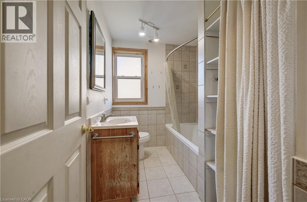 Bathroom featuring a single vanity with an integrated sink, bathtub, built-in shelving, and a window - 174 Bridgeport Road E, Waterloo, ON