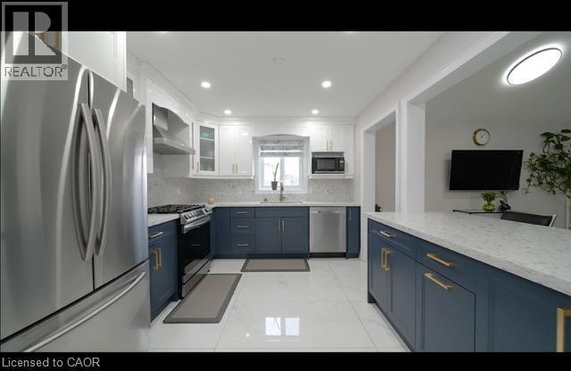 Modern kitchen featuring two-tone cabinetry, stainless steel appliances, a large center island with a stone-finish countertop, and recessed lighting - 643 Doon South Drive, Kitchener, ON