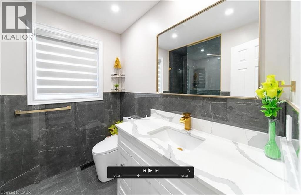 White vanity with integrated sink and gold-finish faucet, large framed mirror, and dark grey tile flooring - 643 Doon South Drive, Kitchener, ON