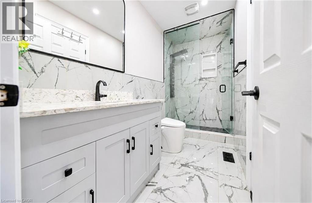 White shaker-style vanity with dark hardware, stone countertop, matte black faucet, full-height tiled shower with glass enclosure, and tiled flooring - 643 Doon South Drive, Kitchener, ON