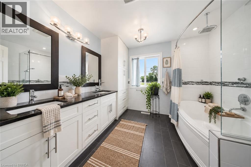 Dual vanity with integrated sinks, dark countertop, white cabinetry, separate walk-in shower with glass enclosure, and a built-in tub - 61 Sunnyside Drive, St. George, ON