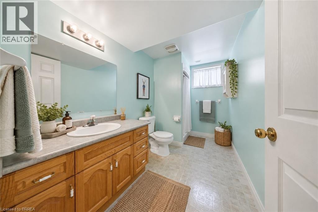 Bathroom featuring a wood-finish vanity with an integrated sink, a large wall-mounted mirror, and a three-light fixture - 61 Sunnyside Drive, St. George, ON