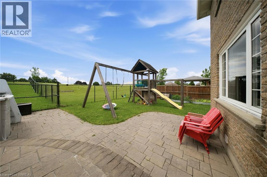 Brick exterior with large windows, paver patio, and grassy yard with play structure - 61 Sunnyside Drive, St. George, ON