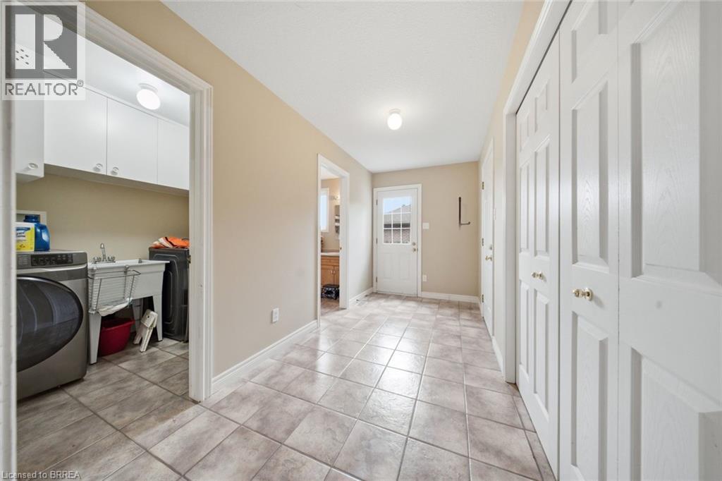 Tile flooring throughout, white bi-fold closet doors, laundry room with built-in cabinetry, utility sink, and washer/dryer hookups, and exterior door with window panes - 61 Sunnyside Drive, St. George, ON