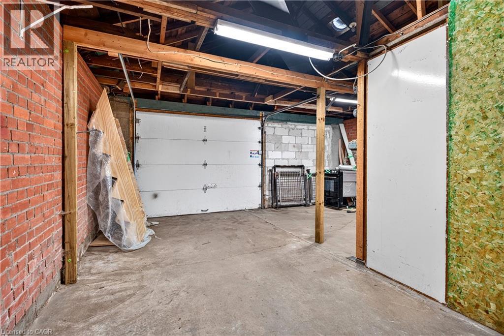 Exposed brick wall, concrete flooring, exposed wood beam ceiling, white paneled garage door, and bright overhead lighting - 689 E Barton Street E, Hamilton, ON