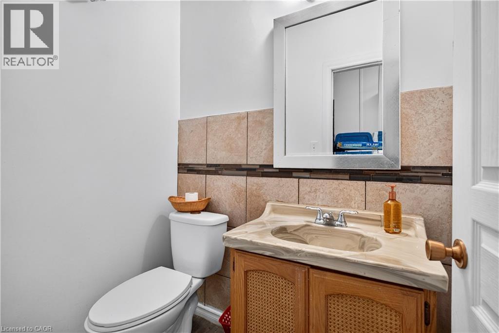 Bathroom featuring a single vanity with an integrated sink, polished chrome faucet, wood-finish cabinet, wall-mounted mirror, and tile wainscoting - 689 E Barton Street E, Hamilton, ON