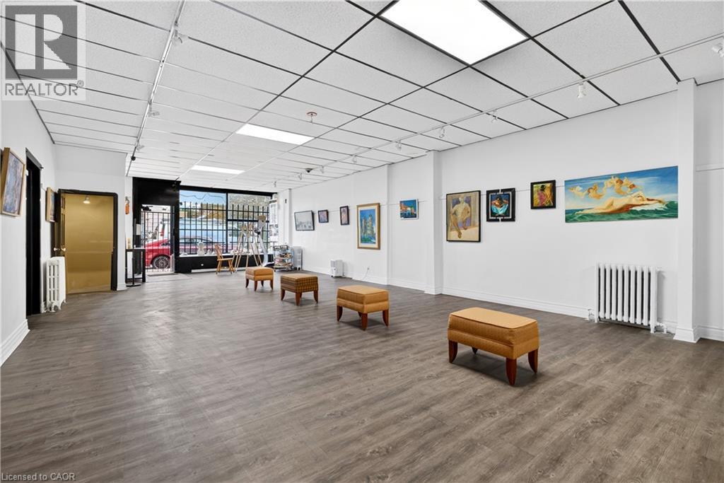 Spacious interior featuring wood-finish flooring, drop ceiling with recessed lighting, track lighting, and a large front window - 689 E Barton Street E, Hamilton, ON