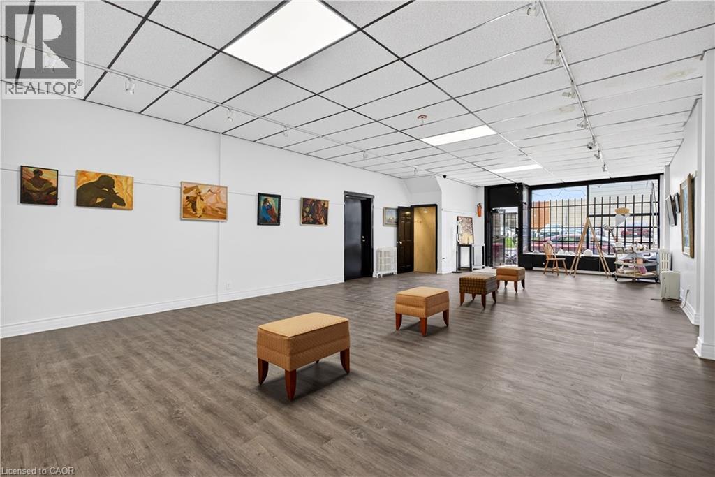 Wide-plank wood-finish flooring, drop ceiling with integrated lighting, track lighting, and a prominent front window - 689 E Barton Street E, Hamilton, ON