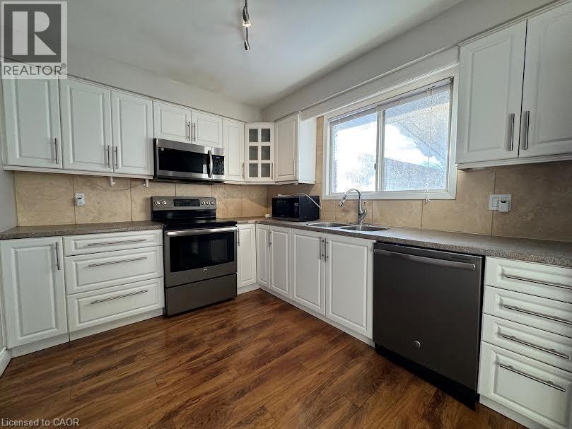 White shaker-style cabinetry with brushed nickel hardware, stainless steel appliances, wood-finish flooring, and a tiled backsplash - 511 Havelock Drive, Waterloo, ON