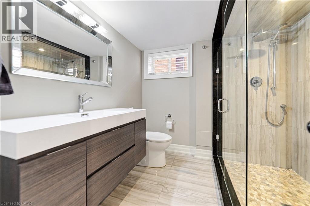 Floating wood-finish vanity, glass-enclosed shower with a rainfall showerhead, and a pebble tile shower floor. Neutral ceramic flooring. - 58 Uplands Avenue, Hamilton, ON