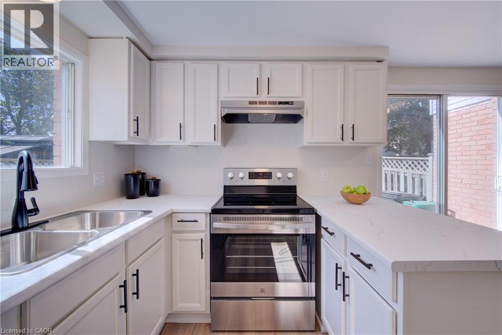 White cabinetry with matte black hardware, stainless steel sink, black gooseneck faucet, stainless steel electric range, and light-toned countertops - 39 Connelly Drive, Kitchener, ON