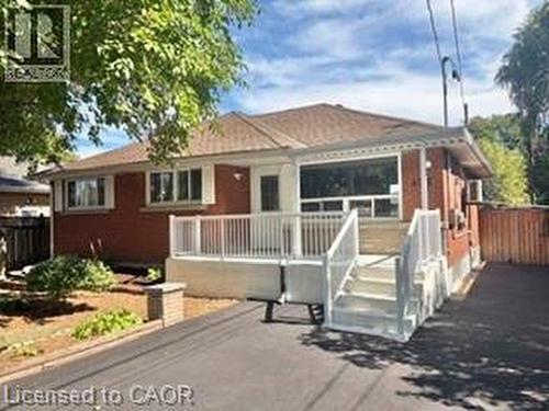 Red brick exterior with white trim, featuring a front deck with white railings and steps - 499 East 16Th Street, Hamilton, ON 