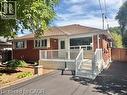 Red brick exterior with white trim, featuring a front deck with white railings and steps - 499 East 16Th Street, Hamilton, ON 