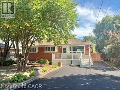 Red brick exterior featuring a front deck with white railings, a paved driveway, and mature landscaping - 499 East 16Th Street, Hamilton, ON 