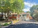 Red brick exterior featuring a front deck with white railings, a paved driveway, and mature landscaping - 499 East 16Th Street, Hamilton, ON 