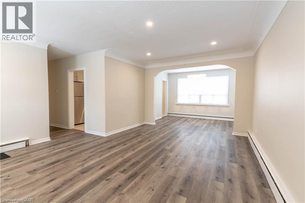 Spacious room with wood-finish flooring, recessed lighting, crown molding, and an arched entryway - 499 East 16Th Street, Hamilton, ON