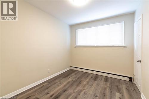 Neutral painted walls, wood-finish flooring, a baseboard heating unit, and a single light fixture - 499 East 16Th Street, Hamilton, ON 
