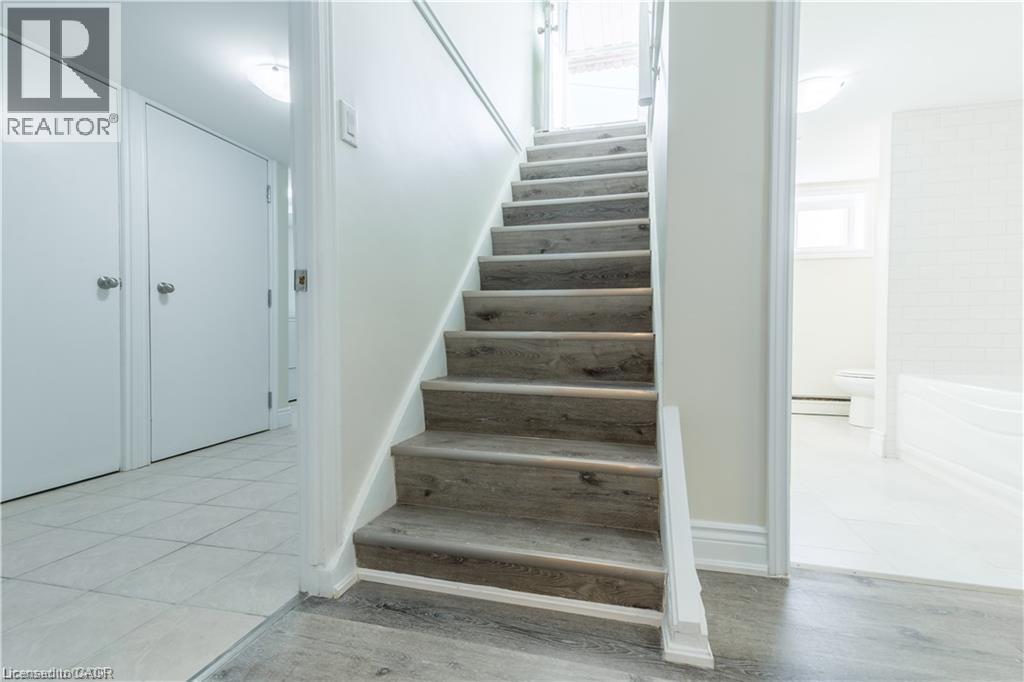 Wood-finish staircase, white interior doors, and light tile flooring - 499 East 16Th Street, Hamilton, ON