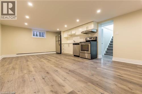 Spacious area featuring wood-finish flooring, recessed lighting, and a kitchen with stainless steel appliances and white cabinetry - 499 East 16Th Street, Hamilton, ON 