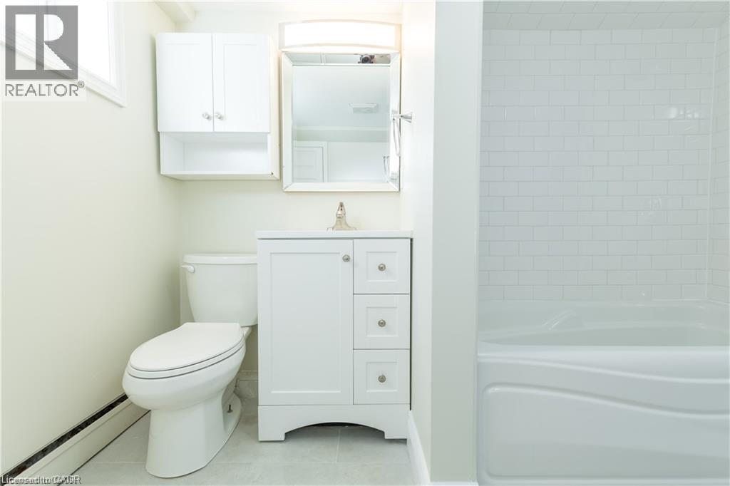 Bathroom featuring white subway tile shower surround, single vanity with integrated sink, white cabinetry with silver hardware, and a wall-mounted medicine cabinet - 499 East 16Th Street, Hamilton, ON