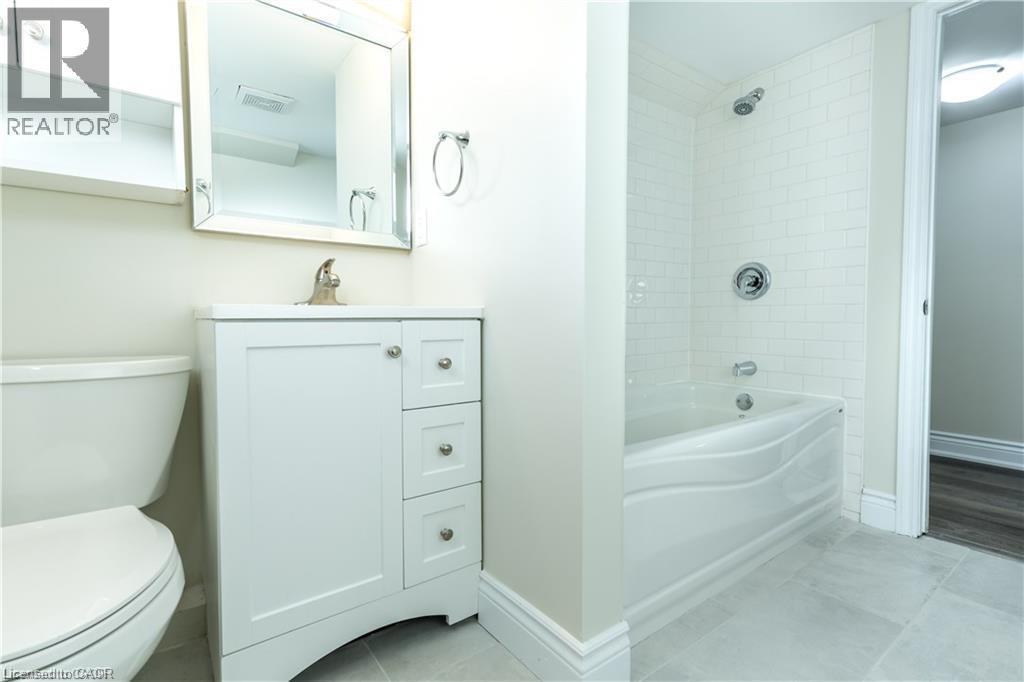 White vanity with brushed nickel hardware, mirror with silver-finish frame, subway tile shower surround, integrated bathtub, and light-toned floor tiling - 499 East 16Th Street, Hamilton, ON