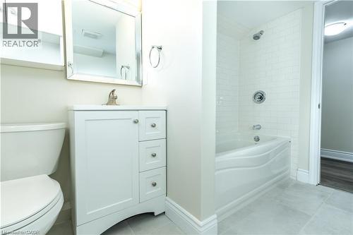 White vanity with brushed nickel hardware, mirror with silver-finish frame, subway tile shower surround, integrated bathtub, and light-toned floor tiling - 499 East 16Th Street, Hamilton, ON 