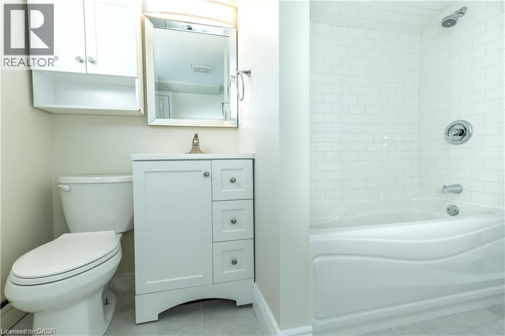 White subway tile bath surround, white built-in tub, white vanity with storage, wall-mounted mirrored medicine cabinet, and white wall-mounted storage cabinet - 499 East 16Th Street, Hamilton, ON