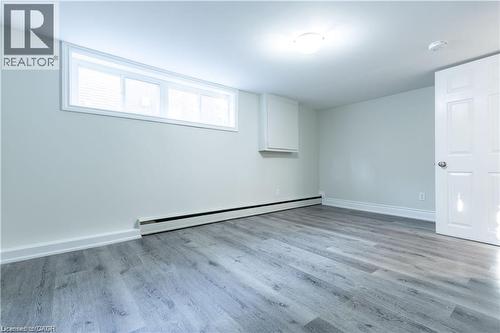 Wood-finish flooring, white trim, horizontal window, white flush-mount ceiling light, and a white door with a silver knob - 499 East 16Th Street, Hamilton, ON 