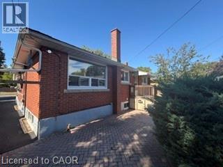 Brick exterior with multiple windows, a prominent chimney, and a paved driveway leading to the rear - 499 East 16Th Street, Hamilton, ON